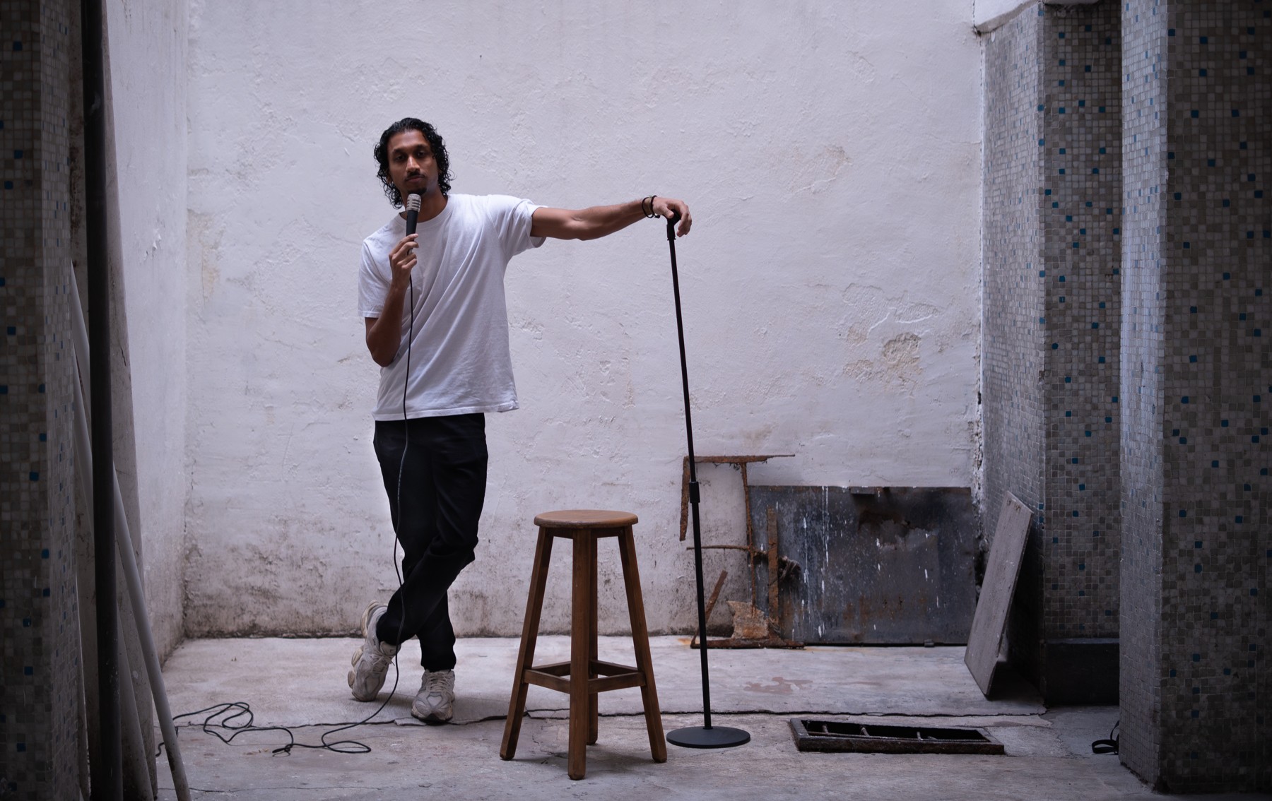 Rah Nimmy standing beside a stool and microphone stand in a sunlit courtyard