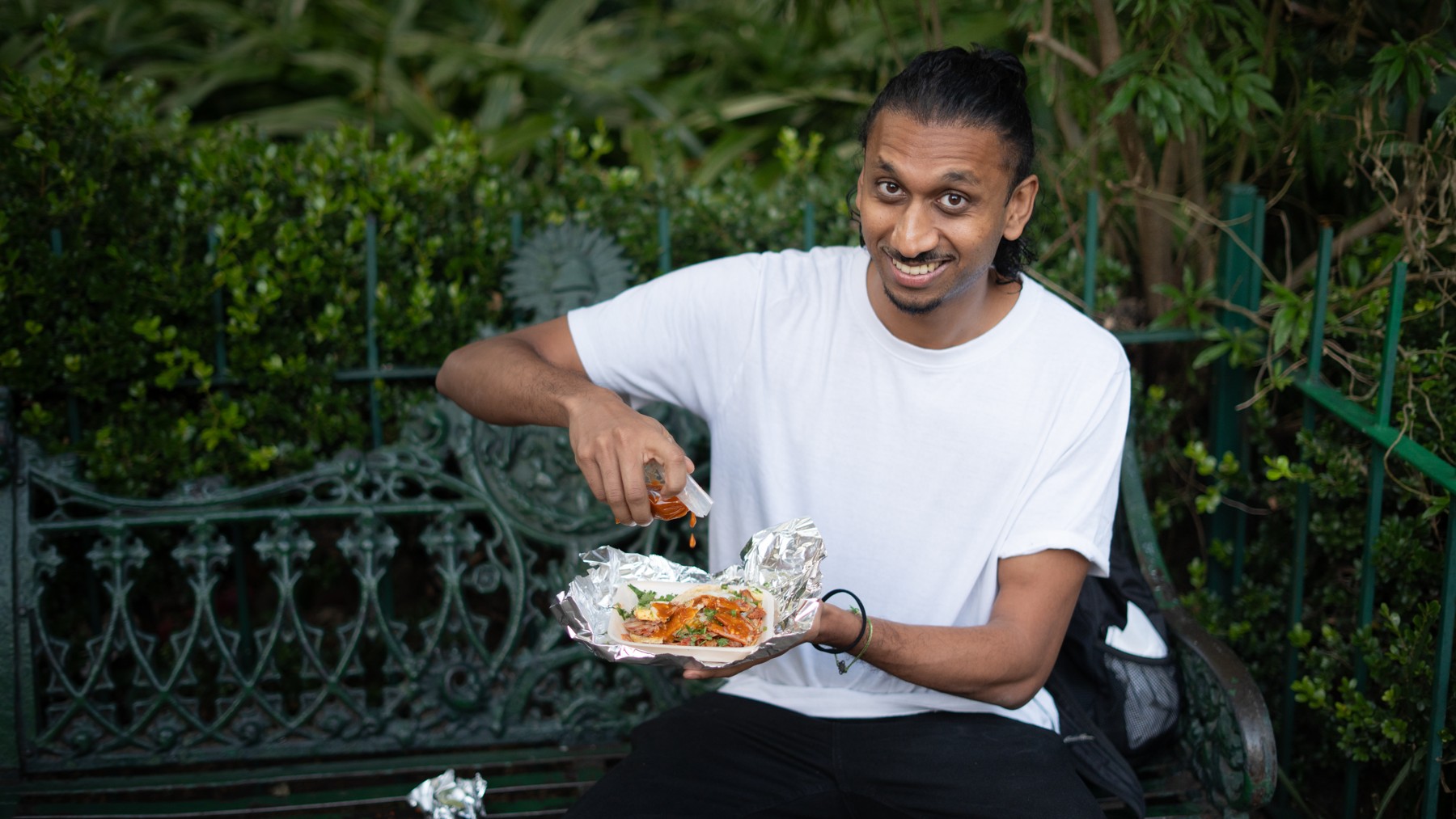 Rah Nimmy smiling while eating outdoors on a park bench
